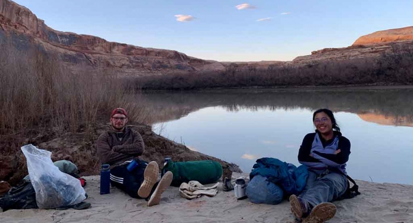 Two people rest on a rock beside a body of water in the Southwest